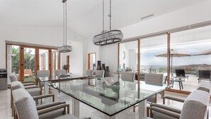 A modern dining area with a glass table and grey upholstered chairs, large windows, and a view of the outdoors. -  Gorgeous estate in Puerto Los Cabos golf and beach community (San José del Cabo)