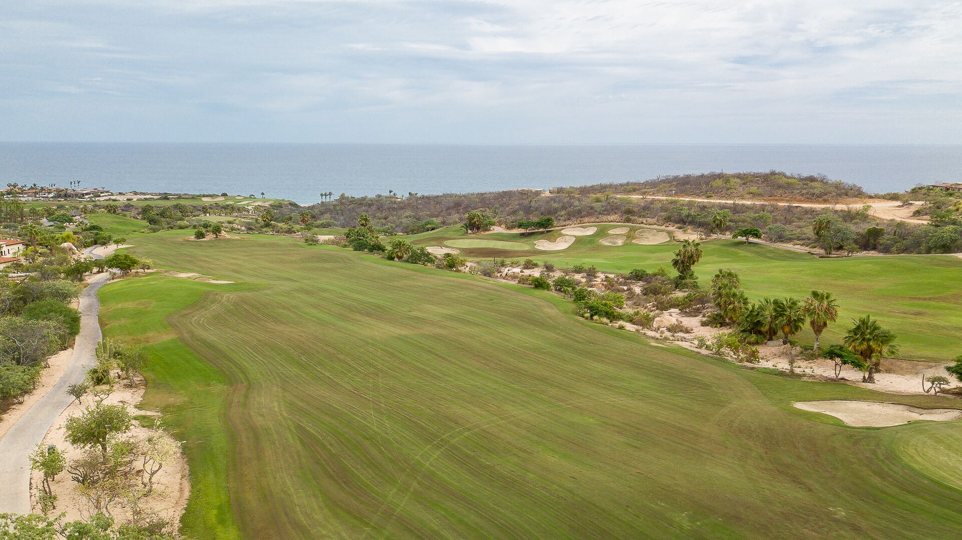 Un parcours de golf offrant une vue sur la côte, avec des bunkers de sable et un chemin pavé.