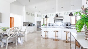 A spacious kitchen with white cabinetry, a central island with stools, stainless steel appliances, and pendant lighting. -  Gorgeous estate in Puerto Los Cabos golf and beach community (San José del Cabo)