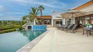 A modern outdoor pool area with a clear blue pool, lounge chairs, and umbrellas. -  Gorgeous estate in Puerto Los Cabos golf and beach community (San José del Cabo)