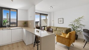 A modern kitchen with a central island, a dining area with a sofa and chairs, and a large window with a view.
