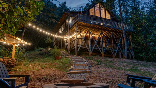 Eine Holzhütte mit einer Terrasse, umgeben von Bäumen und einem Kiesweg, der zu Sitzgelegenheiten im Freien führt.