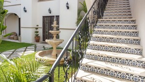 Una escalera con baldosas de diseño azul y blanco, barandilla de hierro forjado y una fuente en el patio.