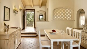 Un espace repas avec une table et des chaises blanches, un buffet avec des verres à vin, et une vue sur l’extérieur grâce à une porte ouverte.