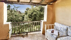 Un balcon donnant sur des arbres, avec un canapé blanc et un magazine.