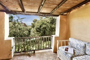 Un balcon donnant sur des arbres, avec un canapé blanc et un magazine.
