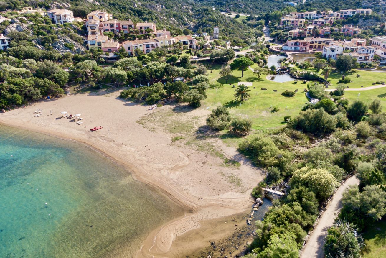 Vue aérienne d’une zone côtière avec une plage de sable, une eau claire et une végétation luxuriante environnante.