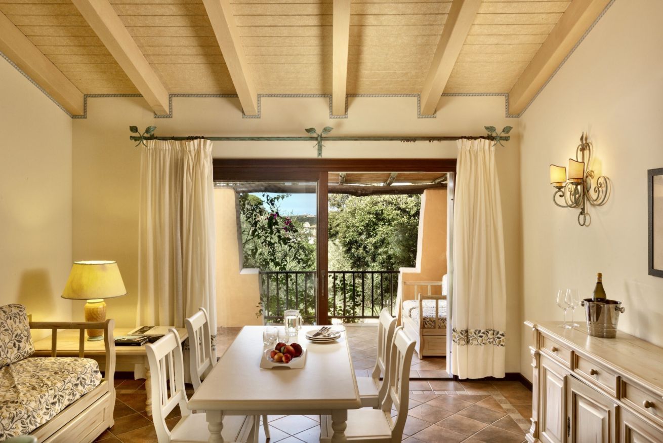 A dining area with a table set for two, a sofa, and a lamp.