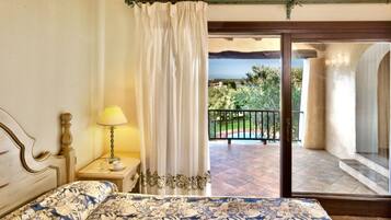 A bedroom with a bed, a nightstand, a lamp, and a view of a balcony with a pool.