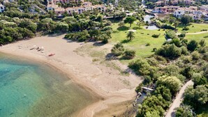 Vue aérienne d’une zone côtière avec une plage de sable, une eau claire et une végétation luxuriante environnante.