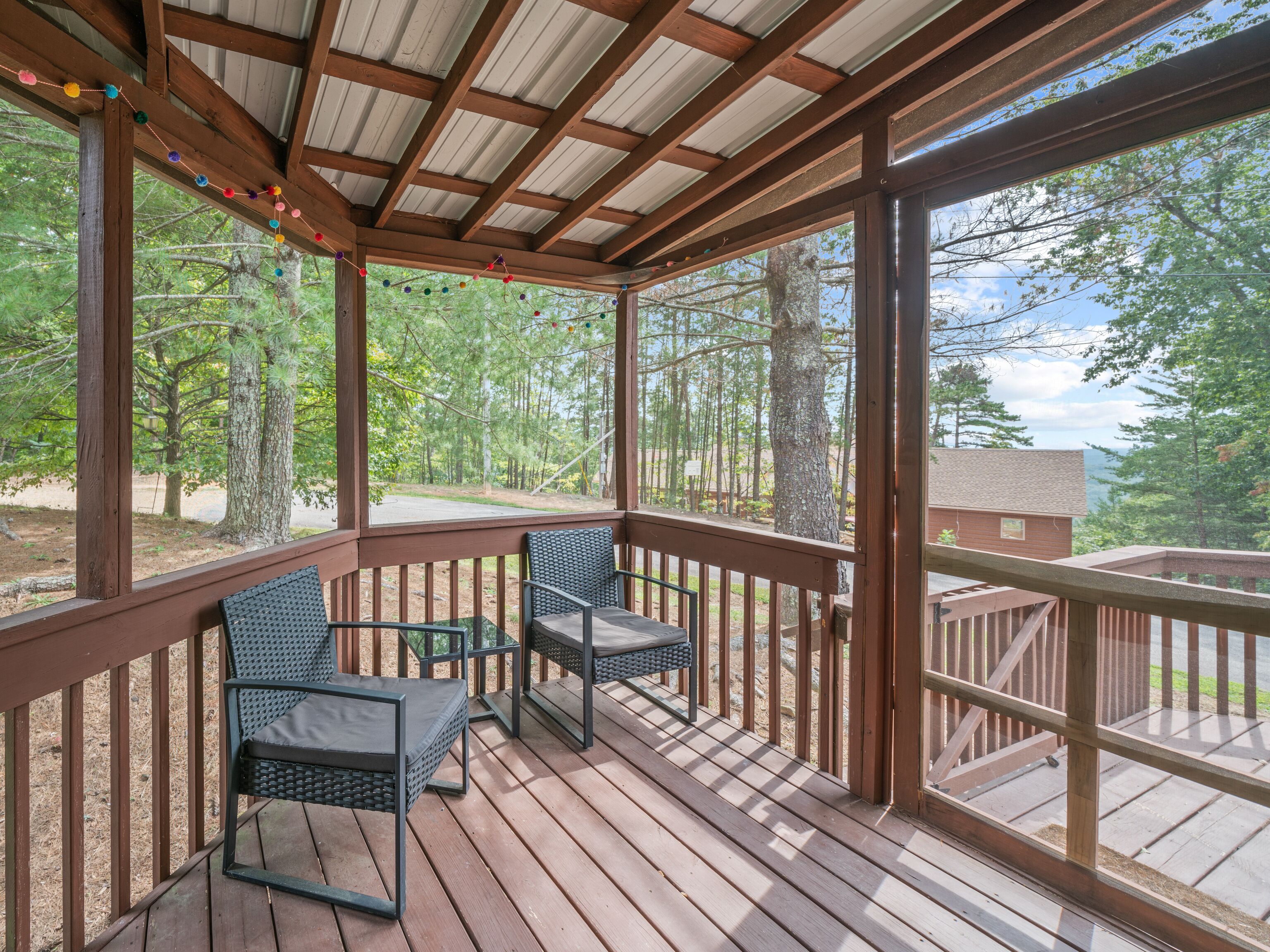 A wooden deck with two wicker chairs and a view of a forest.