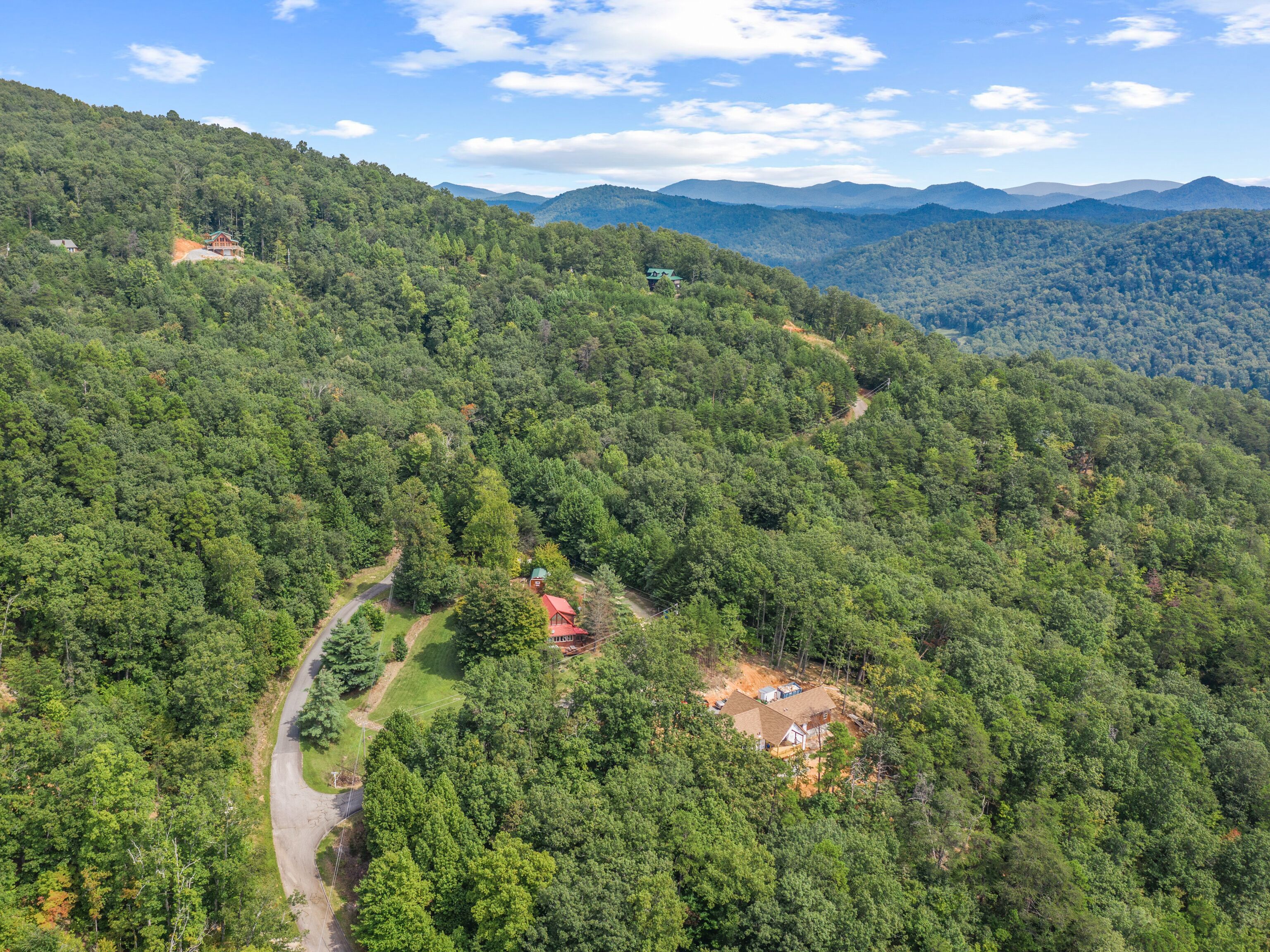 Eine abgelegene Holzhütte, umgeben von dichtem Wald, mit einer kurvenreichen Straße davor.