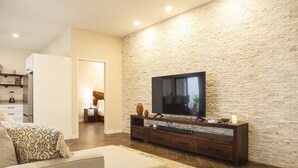 A modern living room with a stone wall, a flat-screen TV, a sofa, and a wooden entertainment unit. - Casa Ixchel | A Modern Mexican Oasis | Private Pool (San Miguel de Cozumel)
