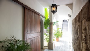 A hallway with a wooden door, potted plants, a tiled floor, and a stone wall with carvings. - Casa Ixchel | A Modern Mexican Oasis | Private Pool (San Miguel de Cozumel)