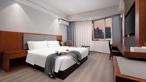 Habitación de hotel moderna con una cama grande, un escritorio, una silla, un televisor y vistas a la ciudad.