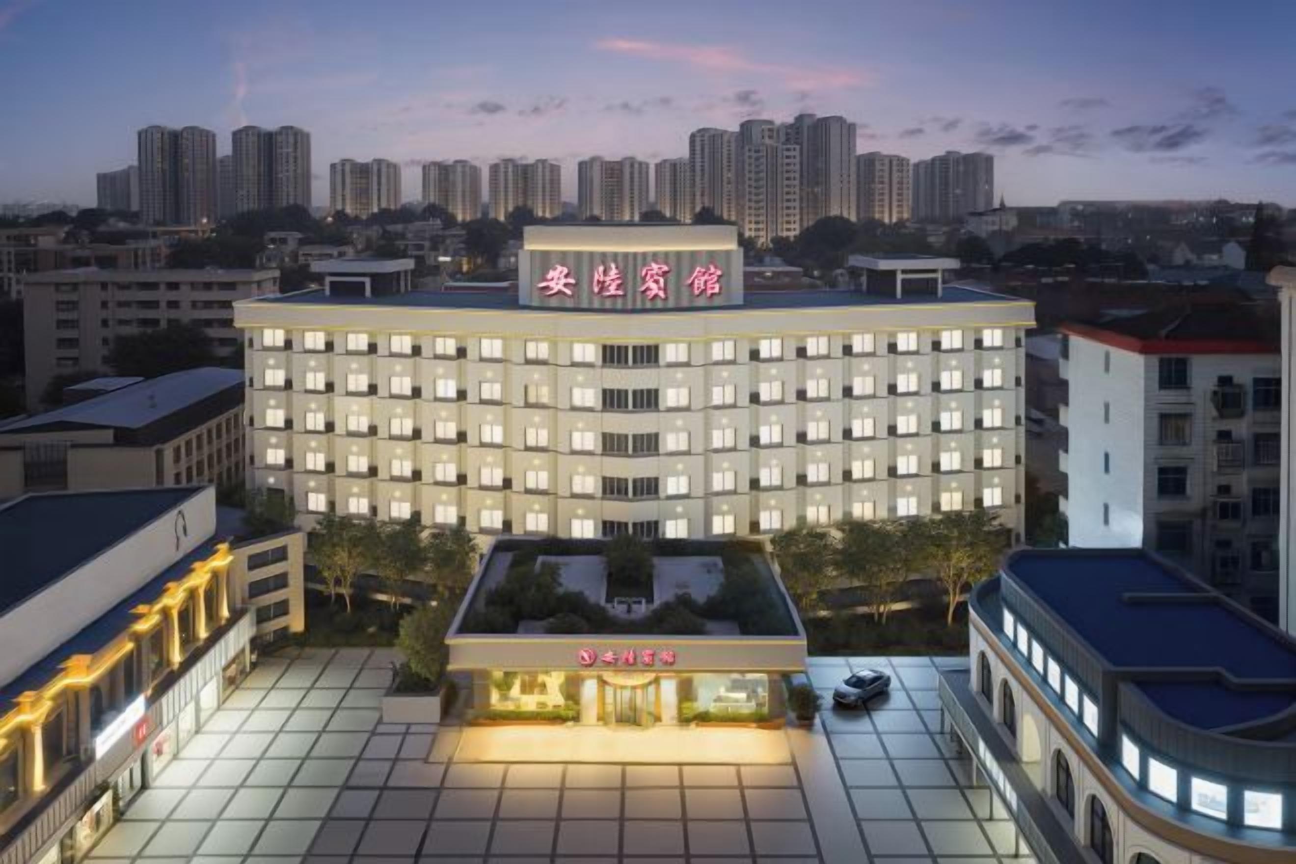 A multi-story hotel with a prominent sign, a courtyard with a seating area, and a view of the surrounding cityscape.