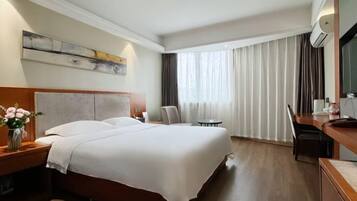 Una habitación de hotel con una cama grande, un escritorio, una silla, una mesita y una ventana con cortinas.