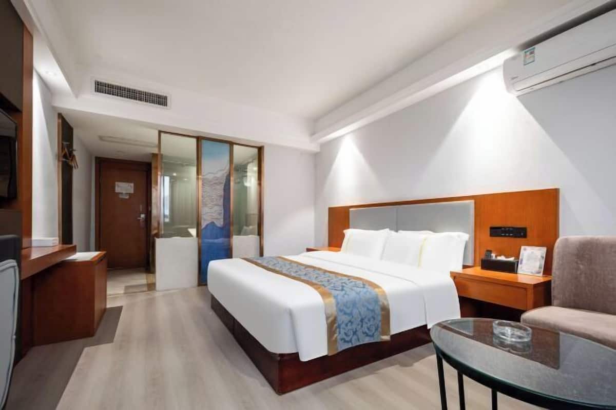 A hotel room with a bed, bedside table, chair, and a small table with a glass.