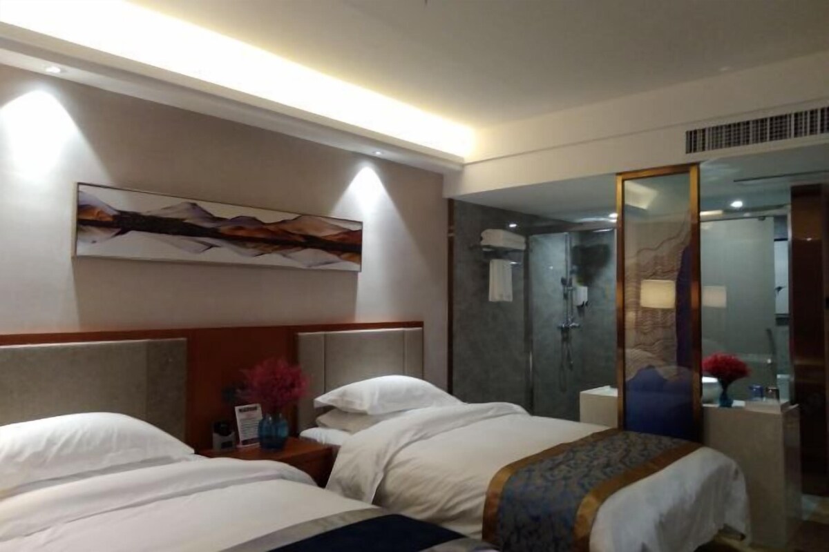 Hotellihuone, jossa on kaksi sänkyä, suuri peili, suihkutila ja taulu seinällä.