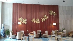 Un moderno vestíbulo de hotel con un muro panelado rojo, una gran obra de arte abstracta dorada en la pared y una zona de estar con mesas y sillas redondas.