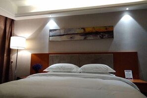 Una habitación de hotel con cama, mesita de noche, lámpara y un cuadro en la pared.