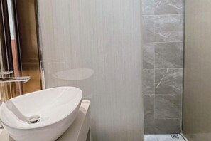 A modern bathroom with a white vessel sink, a glass shower enclosure, and marble tiles. - Anlu Hotel (Anlu)