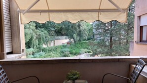 Un balcó amb vista a un jardí, una taula petita amb una planta i dues cadires.