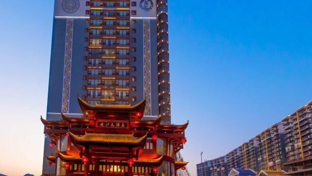 Un hôtel de grande hauteur dont la base présente un style architectural chinois traditionnel, avec une entrée imposante ornée de lanternes rouges.