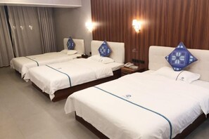 A hotel room with three single beds, each with a blue pillow and a white bedspread. There are two bedside tables with lamps, and the room has wooden paneling on the walls. - Gujiang Hotel (Dahua)