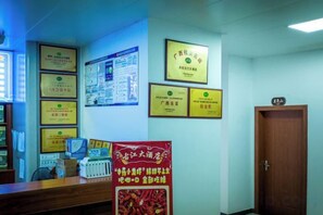 A reception area with framed certificates on the wall, a wooden reception desk, and a closed door. - Gujiang Hotel (Dahua)