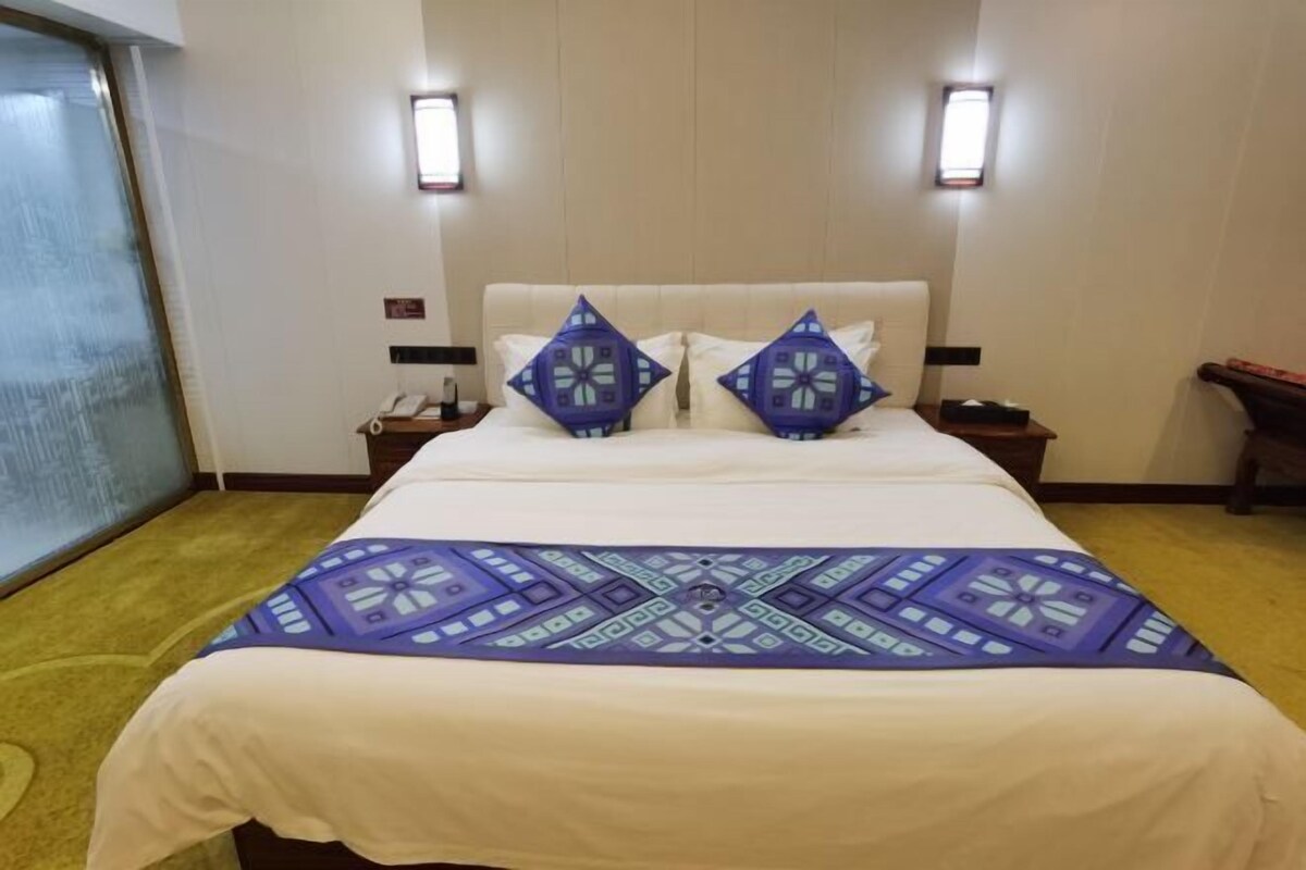 A hotel room with a large bed, two bedside tables with lamps, and a window with a view.