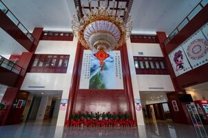 Un vestíbulo amplio con una gran araña, un mural central y una zona con alfombra roja.