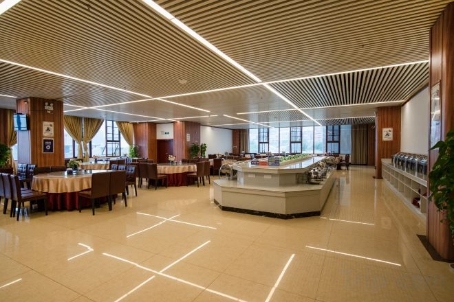 Un amplio espacio interior con mesas y sillas dispuestas para comer, una barra central y un diseño moderno del techo.