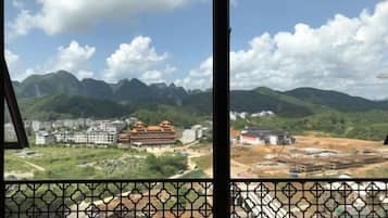 Une vue à travers une fenêtre ornée d’un motif géométrique, donnant sur un paysage montagneux avec des bâtiments et des chantiers de construction.