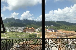 A view through a window with a geometric pattern, overlooking a mountainous landscape with buildings and construction sites. - Gujiang Hotel (Dahua)