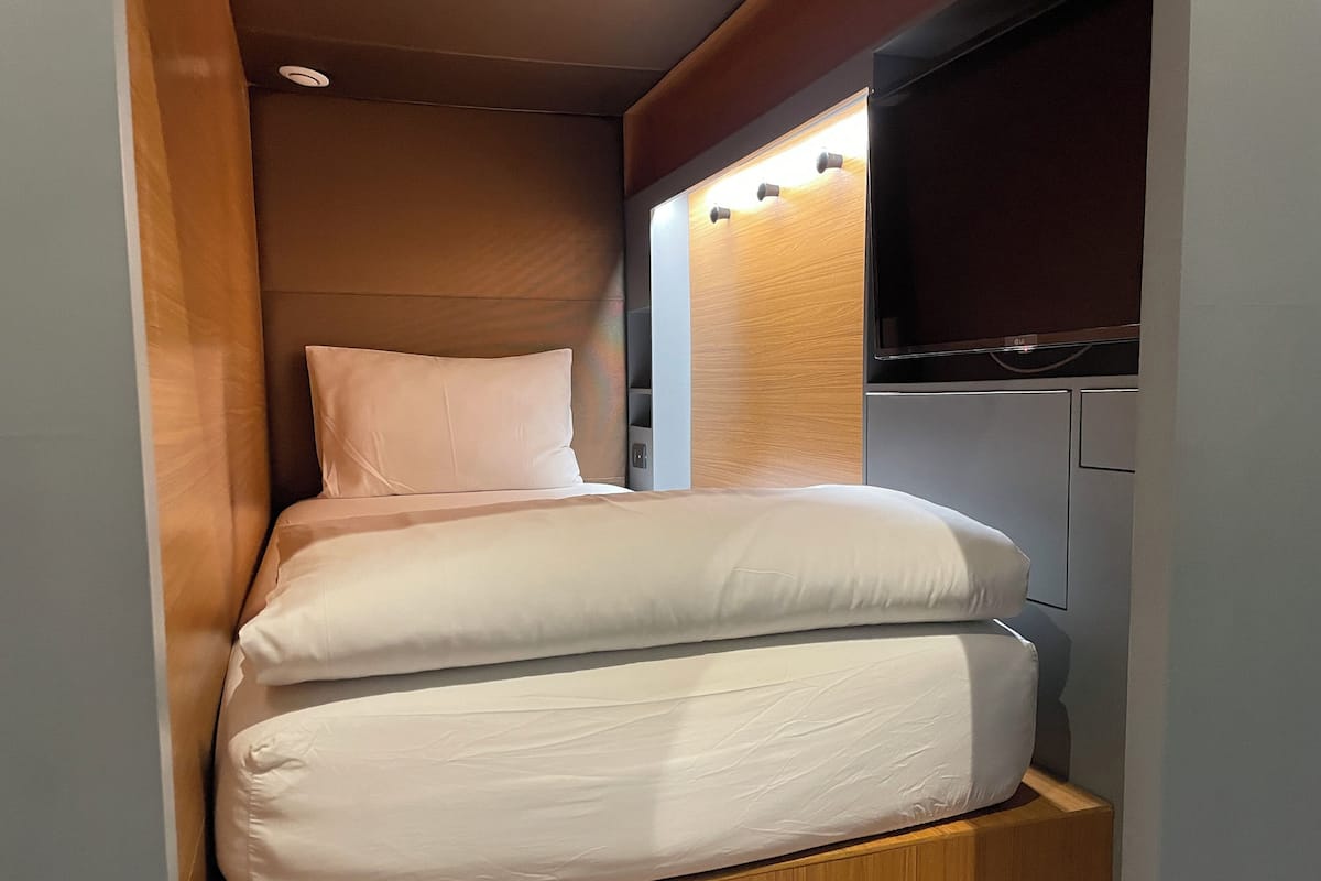 A compact bed with two pillows in a cabin-like space with wooden paneling and a small window.