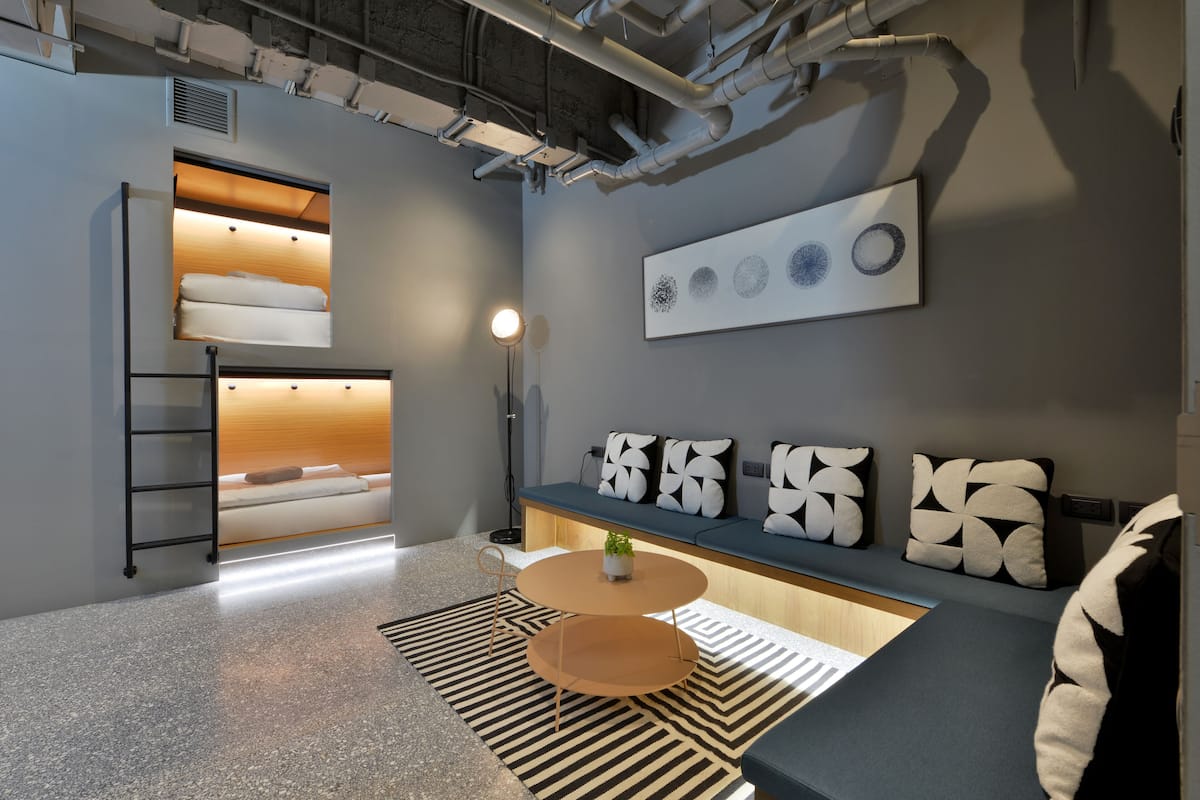 A modern, compact living space with a loft bed, a sofa, a coffee table, and a wall-mounted artwork.