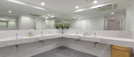 A modern bathroom with three sinks, a large mirror, and a small plant.