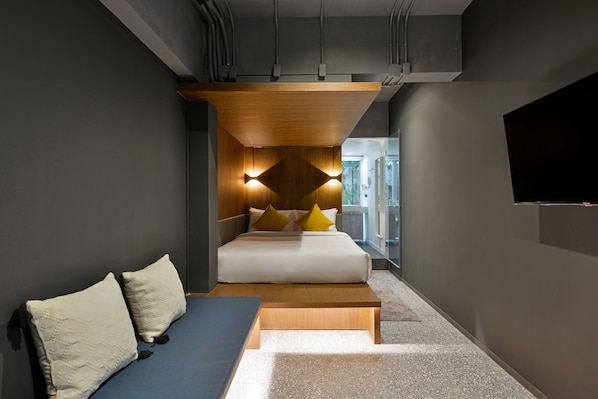 Une chambre d’hôtel moderne équipée d’un lit, d’un canapé et d’un téléviseur fixé au mur.