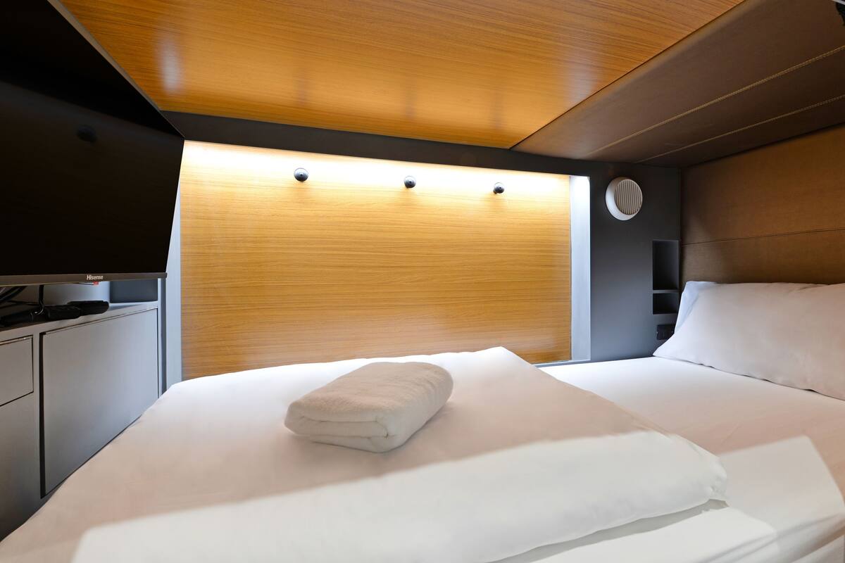 A modern hotel room with a neatly made bed, a flat-screen TV, and a wooden headboard.
