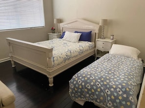 Double and single beds with matching headboards and dressers, plus a window with blinds.