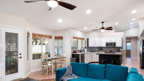 A modern kitchen with white cabinets, a central island, and a dining area with a table and chairs. - Arrowhead Family Getaway Pool Pet Friendly (Peoria)