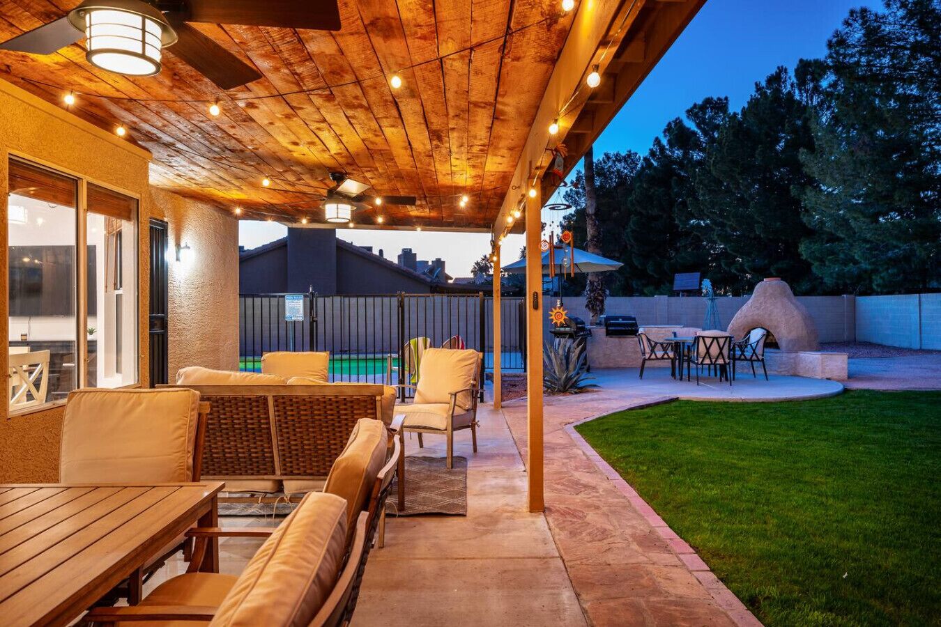 Eine überdachte Terrasse mit Gartenmöbeln, einem Grill und einem Schwimmbad im Hintergrund.