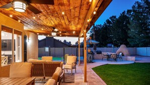 A covered patio with outdoor furniture, a grill, and a swimming pool in the background. - Arrowhead Family Getaway Pool Pet Friendly (Peoria)