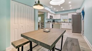 A modern kitchen with white cabinets, a wooden dining table, and pendant lighting. - Updated North Beach Cottage: Pet Friendly! (North Beach)