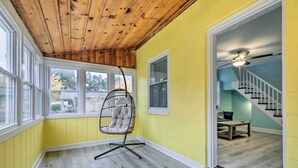 A room with a hanging chair, wooden ceiling, large windows, and a staircase leading to another level. - Updated North Beach Cottage: Pet Friendly! (North Beach)
