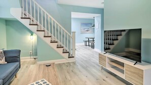 A modern living room with a staircase, a flat-screen TV, and a dining area. - Updated North Beach Cottage: Pet Friendly! (North Beach)