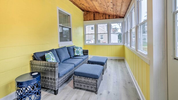 A sunlit room with a wicker sofa and ottomans, a small round table, and a window overlooking a street. - Updated North Beach Cottage: Pet Friendly! (North Beach)