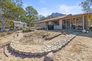 Una casa moderna con un porche cubierto, una zona de barbacoa y un camino de piedra que lleva a la entrada.