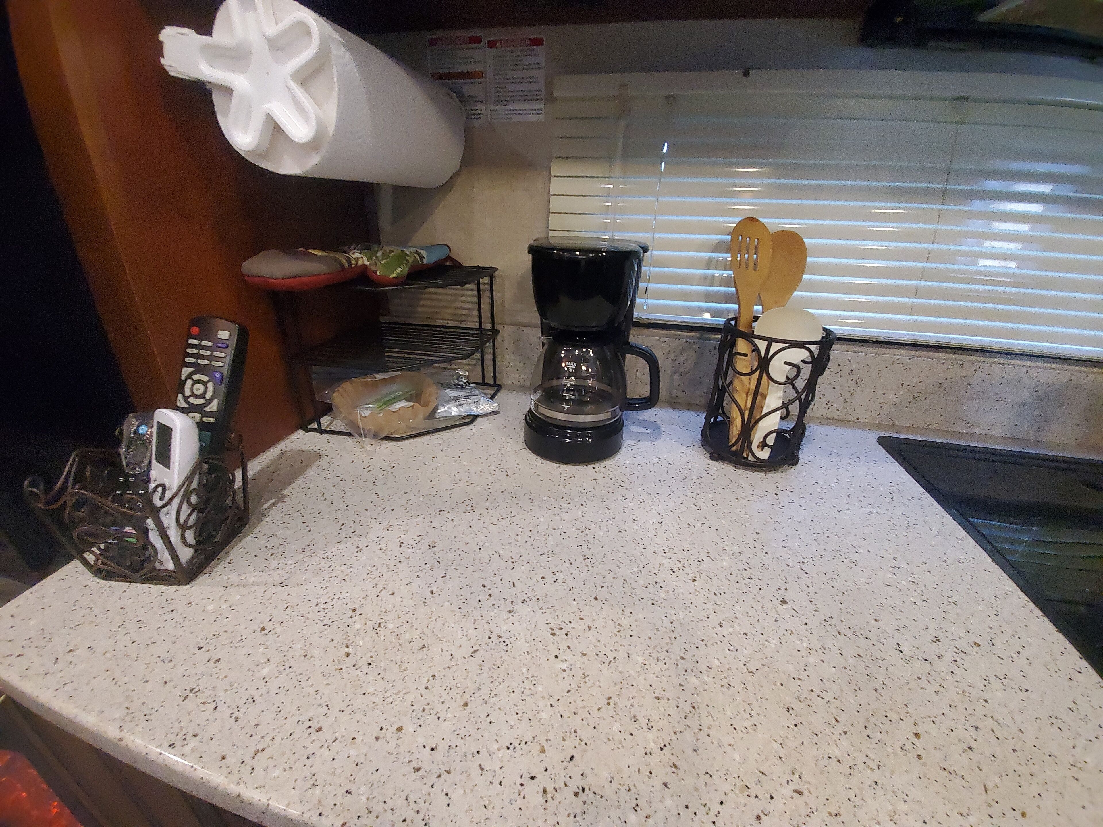 Una encimera de cocina con una cafetera, una cesta de utensilios y un control remoto.